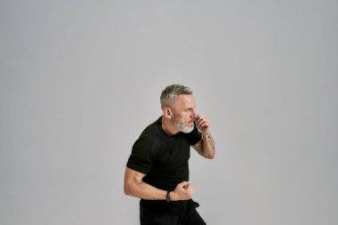 Siyah spor giyim boksu içinde orta yaşlı bir sporcu. Stüdyoda gri arka plan üzerinde egzersiz yaparken yumruk pratiği yapıyor.