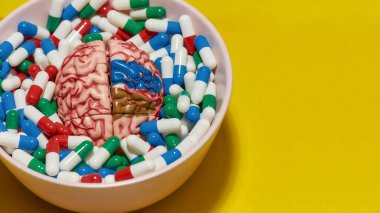 Farklı ilaç içeren yaratıcı konsept, sarı arka planda insan beyni modeli olan kapsüller. Sağlık ve tedavi kavramı
