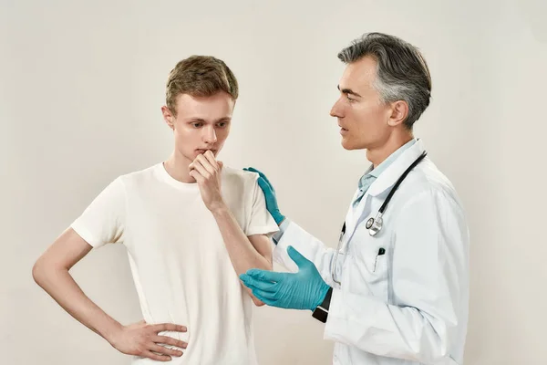 Rossz hírek. Érett professzionális orvos orvosi egyenruhában és kék steril kesztyű beszél aggódó fiatal férfi beteg, magyarázó diagnózis — Stock Fotó