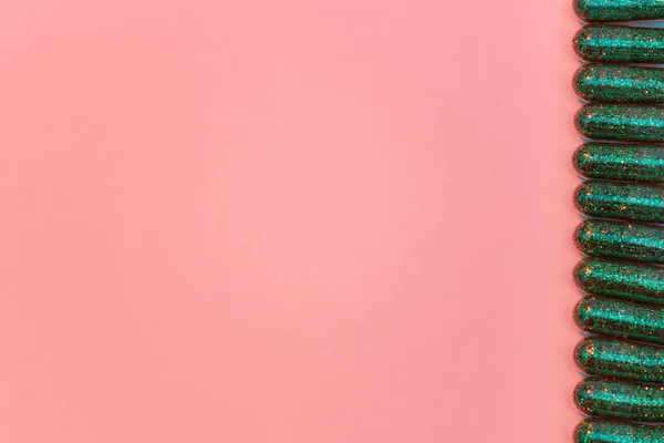 Creatief concept met veel groene glitter pillen liggend in een rij verticaal geïsoleerd op pastel roze achtergrond. Minimale stijl, kunstconcept — Stockfoto