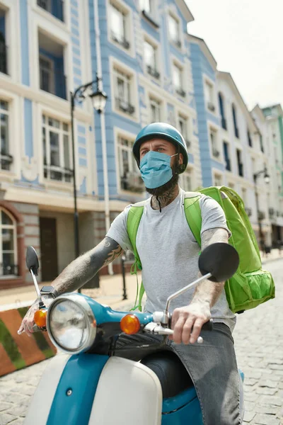 Everything at your doorstep. Delivery man in helmet wearing mask due to the emergence of the Covid19 virus, riding a motor scooter, delivering food. Courier, delivery service, lockdown concept