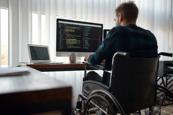Çoklu görev. Modern ofiste iş yerinde üç monitörle otururken tekerlekli sandalye yazma programı kodlu beyaz erkek web geliştiricisinin geçmişe bakış — Stok fotoğraf