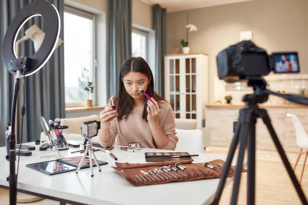 Redefinir la belleza. Blogger asiática mostrando productos cosméticos mientras graba un video tutorial para su blog de belleza usando cámara en casa —  Fotos de Stock