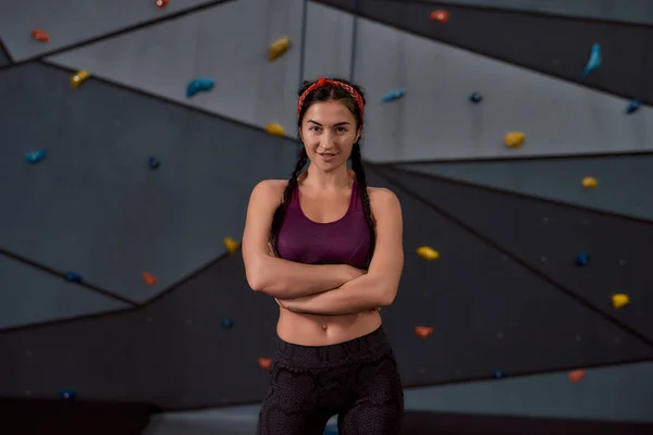 Spor giyim sektöründe aktif genç bir kadın kameraya bakıyor, yapay tırmanma duvarına karşı duruyor. Spor hayatı ve kaya tırmanışı kavramı — Stok fotoğraf