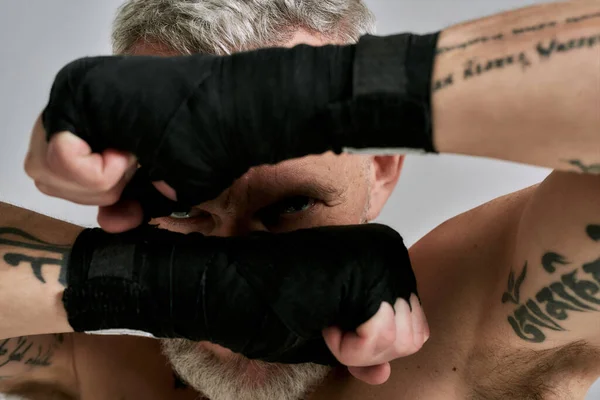 Primo piano di uomo atletico di mezza età, kickboxer nasconde il suo volto dietro le mani avvolte in studio su sfondo grigio. Muay Thai, Boxe o Kickboxing concetto — Foto Stock