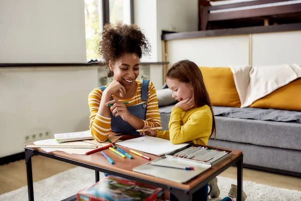 Tapasztalja meg a gyermekgondozás, ahogy kell. Fehér kislány, aki afro-amerikai bébiszitterrel tölti az idejét. Rajzolnak, rajzolni tanulnak, a padlón ülnek. — Stock Fotó