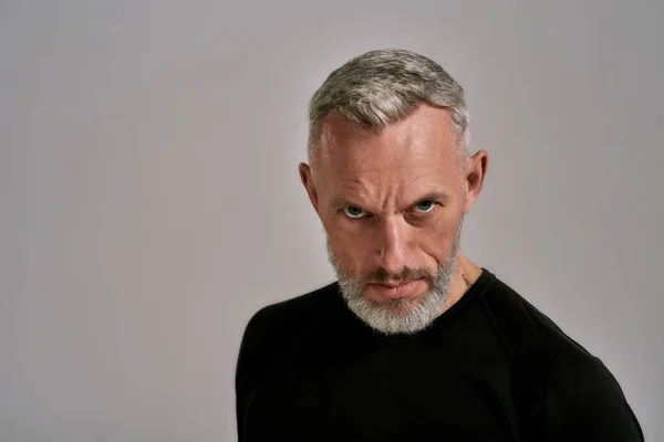 Primer plano del hombre de mediana edad en camiseta negra mirando a la cámara mientras posa en el estudio sobre fondo gris —  Fotos de Stock