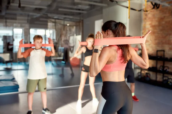 Giovane allenatrice che lavora con la fascia di resistenza in palestra insieme a bambini, adolescenti. Sport, stile di vita sano, educazione fisica — Foto Stock