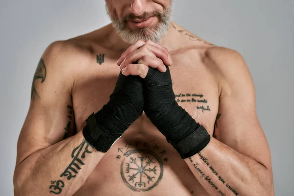 Colpo ritagliato di mezzo nudo uomo atletico di mezza età, kickboxer mani pieghevoli in piedi in studio su sfondo grigio. Muay Thai, Boxe o Kickboxing concetto — Foto Stock