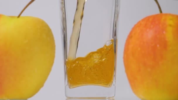 Bio-Saft. Zeitlupenaufnahme des Einfüllens von frischem Apfelsaft in Glas und köstlichen gelben Äpfeln vor weißem Hintergrund — Stockvideo