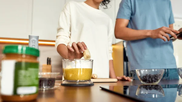 Ζευγάρι ετοιμάζεται υγιεινό ποτό, smoothie μαζί στην κουζίνα. Νεαρή γυναίκα βάζοντας φρούτα στο μπλέντερ, ο άνθρωπος ελέγχοντας συνταγή χρησιμοποιώντας το tablet pc — Φωτογραφία Αρχείου
