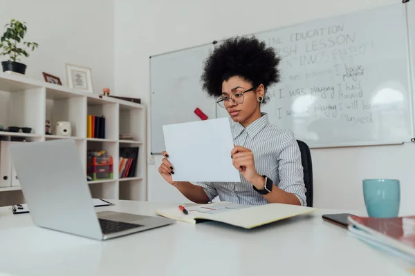 Fiatal afro-amerikai női angol tanár, aki egy üres papírlapot mutat a laptopja webkamerája előtt, miközben online tanul. Koncentrálj egy nőre. — Stock Fotó