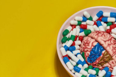 Farklı ilaç içeren yaratıcı konsept, sarı arka planda insan beyni modeli olan kapsüller. Sağlık ve tedavi kavramı