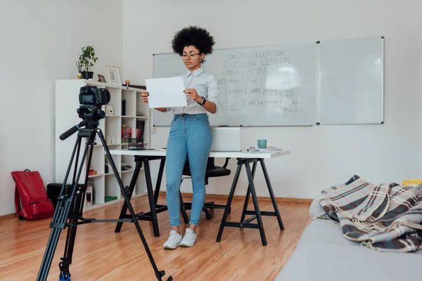 Online tanítás rögzítése. A fókuszált afro-amerikai nő teljes hossza, aki egy üres papírlapot mutat a kamera előtt, miközben angolul tanít online — Stock Fotó