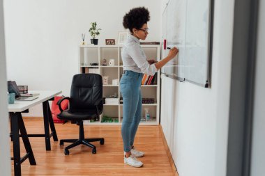 Çevrimiçi sınıf. Beyaz tahtaya günlük giysiler içinde bir şeyler yazan Afro-Amerikan bayan öğretmenler. Evden çevrimiçi öğretim