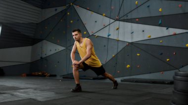 Spor giyim bölümünde, vücudunu esnerken duvara karşı duran genç bir adamın tam boy çekimi. Spor hayatı ve kaya tırmanışı kavramı