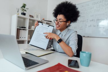 Çevrimiçi dil dersi. Genç mutlu Afro-Amerikan kadın kablosuz kulaklık takıyor web kameralarına bakıyor ve çevrimiçi İngilizce öğretiyor.