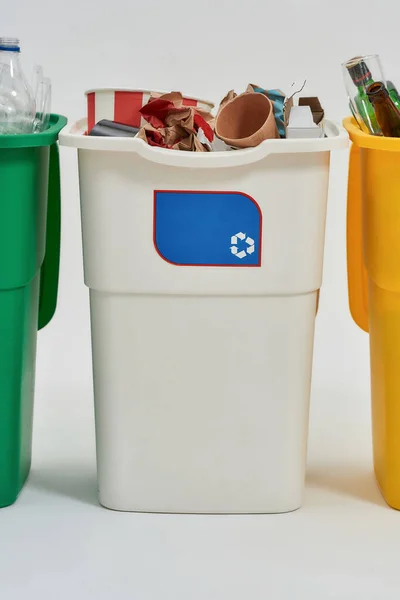 Cubo de basura de reciclaje blanco con cartel de reciclaje en él lleno de basura de pie en una fila con otros contenedores aislados sobre fondo blanco. Concepto de separación de residuos —  Fotos de Stock