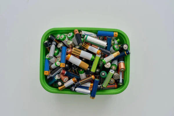 Top view of many alkaline batteries in green plastic container on white background. Concept of recycling waste and environmental pollution — Stock Photo, Image