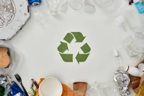 Flatlay composition with different waste, garbage types and recycling sign made of paper in the center over white background