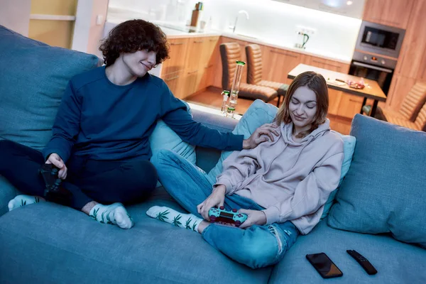 Não se preocupe. Casal jovem jogando videogames depois de fumar maconha de um cachimbo enquanto estava sentado no sofá em casa — Fotografia de Stock