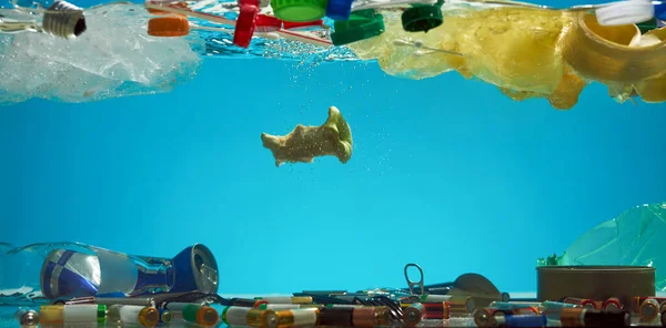 Close up of plastic bags, batteries, food waste and other types of garbage in the blue water. Ecological disaster and pollution of the world ocean concept