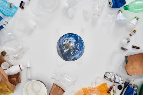 Flatlay složení s různými odpady, typy odpadků a papírový model Země v centru nad bílým pozadím — Stock fotografie