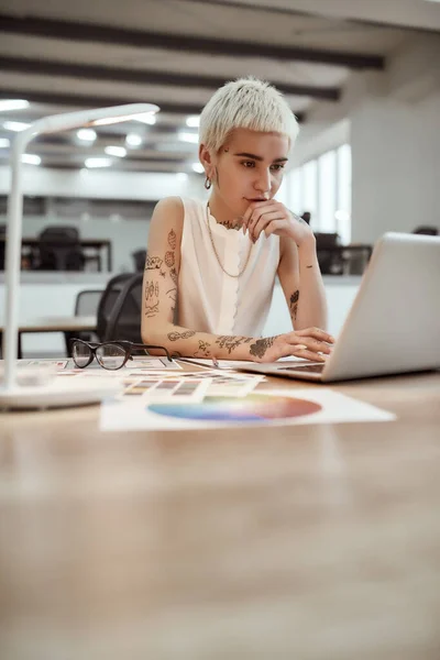 Empresária de sucesso. Bonito e jovem tatuado designer feminino usando laptop enquanto trabalhava em sua mesa no escritório moderno. Designer local de trabalho — Fotografia de Stock