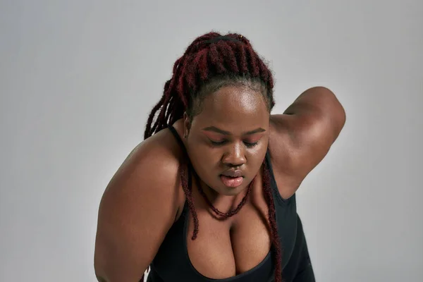 Gros plan de dodu, plus la taille femme afro-américaine en vêtements de sport se fatiguer, épuisé après l'entraînement en studio sur fond gris — Photo