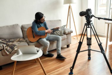 Gitar dersi veriyorum. Genç bir blogcu ya da müzik öğretmeni elinde gitarla kanepede oturuyor ve evde video dersi kaydediyor.