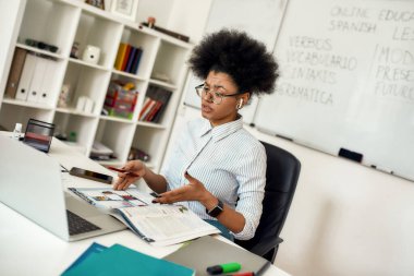 İnternette İspanyolca öğretmeni. Odaklanmış Afro-Amerikalı kadın kablosuz kulaklık takıyor ve evden web kamerasıyla İspanyolca öğretiyor.