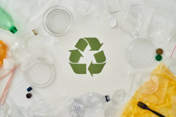 Composição plana com diferentes garrafas de plástico vazias, recipientes e placa de reciclagem feita de papel no centro sobre fundo branco — Fotografia de Stock