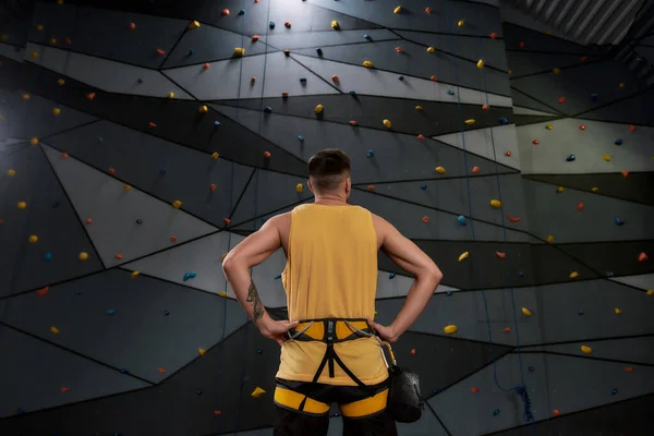 Kampf der Schwerkraft. Junger, sportlicher Mann, Bergsteiger mit einem Sack Magnesia, Kreide an einer künstlichen Kletterwand. Konzept des Sportlebens und Klettern — Stockfoto