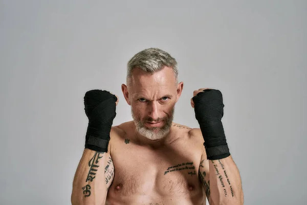 Vägra att förlora. Halv naken medelålders atletisk man, kickboxare ser arg håller händerna stående i studio över grå bakgrund. Muay Thai, Boxning eller Kickboxning koncept — Stockfoto