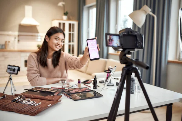 Распространи свое очарование. Женщина-блогер красоты снимает, рекламное приложение на камеру, держит смартфон. Влиятель макияжа азиатская девушка запись косметики обзор продукта на дому — стоковое фото