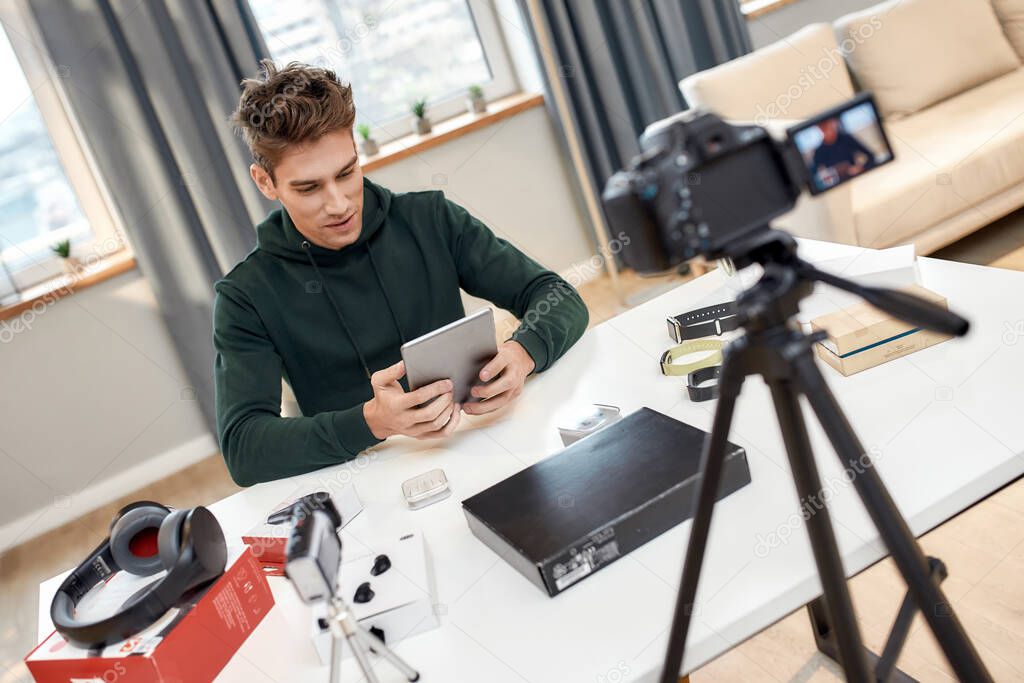 Digital Life. Young male technology blogger recording video blog or vlog about new tablet pc and other gadgets at home studio. Blogging, Work from Home concept
