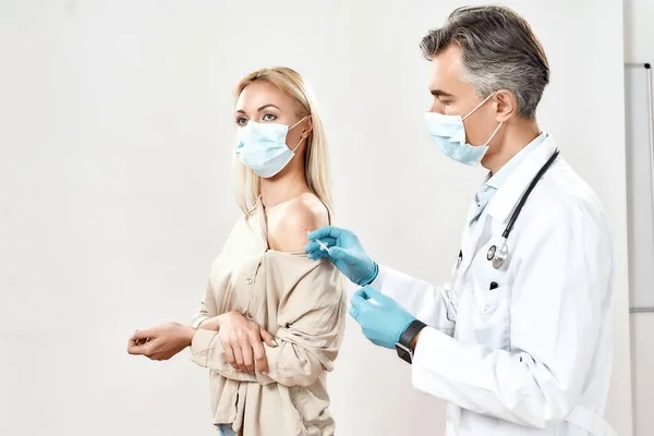 İğne yaptırıyorum. Mavi steril eldivenli erkek doktor tıbbi maske takan genç bayana iğne yapıyor. Aşı, ilaç ve sağlık hizmetleri — Stok fotoğraf