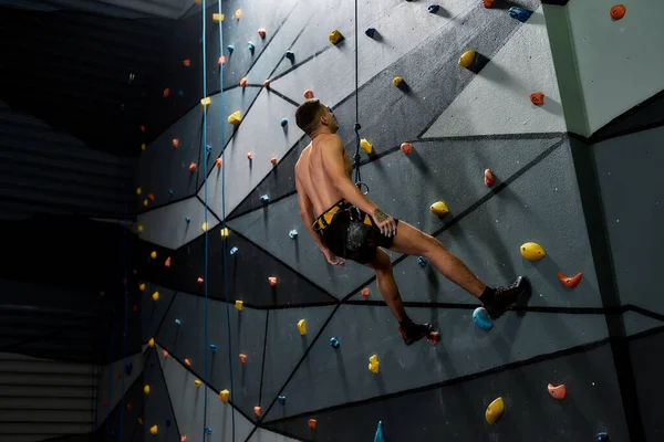 Hombre en equipo de seguridad y arnés teniendo un descanso mientras entrena en la pared de escalada artificial en el interior —  Fotos de Stock