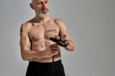 Yarı çıplak orta yaşlı atletik adam, kickboksör Muay Thai, boks veya kickboks için elleri saran, gri arka plan üzerinde stüdyoda duran