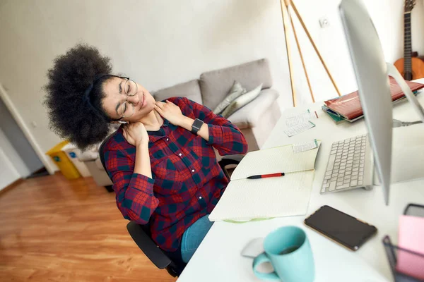 Mi sento stanco dopo aver studiato online tutto il giorno. Giovane donna afro-americana massaggiare il collo e rilassarsi dopo un lungo lavoro al computer sul posto di lavoro a casa — Foto Stock