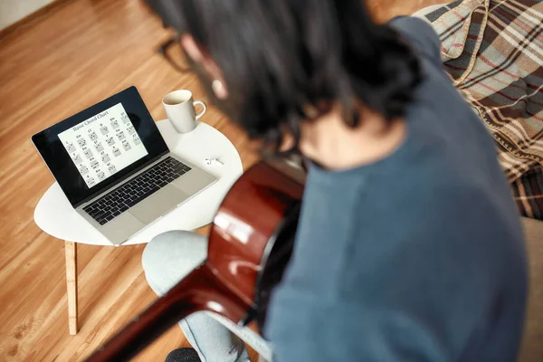 Apprendre la musique en ligne. Vue arrière d'un jeune homme regardant un tutoriel vidéo et pratiquant des accords de guitare à la maison. Auto-isolement — Photo