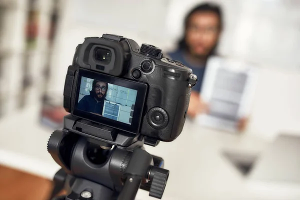 Jeune homme enseignant en ligne, regardant la caméra et expliquant un nouveau thème tout en travaillant à la maison. Focus sur appareil photo, équipement numérique professionnel — Photo