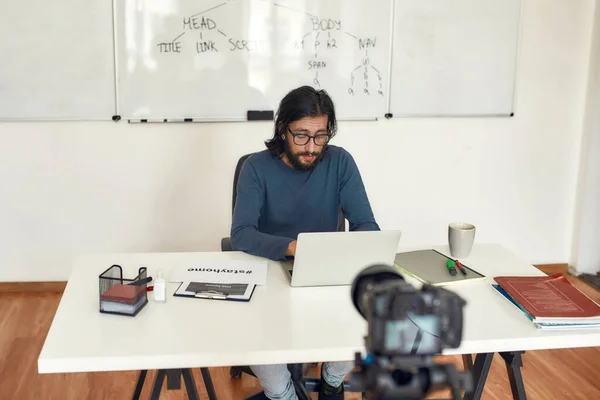 Werken vanuit huis. Gericht mannelijke leraar werken op laptop tijdens het zitten op zijn werkplek en het onderwijzen van computerwetenschap online — Stockfoto