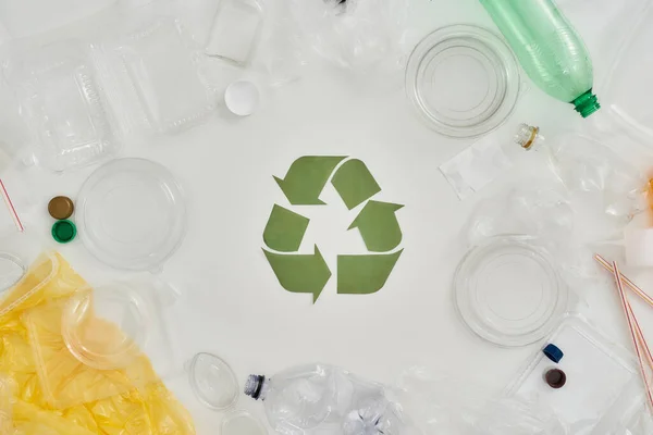 Composição plana com diferentes garrafas de plástico vazias, recipientes e placa de reciclagem feita de papel no centro sobre fundo branco — Fotografia de Stock