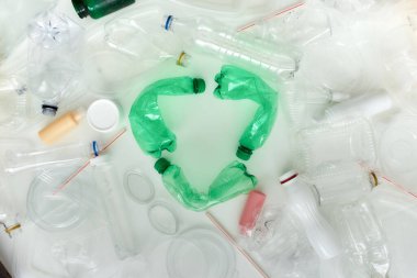 Farklı kullanılmış kaplar ve merkezinde yeşil plastik şişelerden yapılmış geri dönüşüm sembolü olan kavramsal düz yatak. Atık konsepti geri dönüşümü.