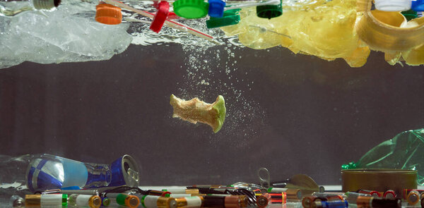 Close up of plastic bags, batteries, food waste and other types of garbage in the dark water. Ecological disaster and pollution of the world ocean concept