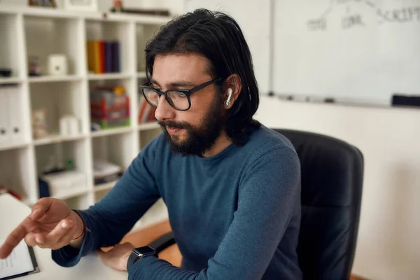 Primer plano de joven barbudo hombre profesor sentado en su lugar de trabajo, mirando a la pantalla de la computadora y dando clase en línea a través de la webcam en casa — Foto de Stock