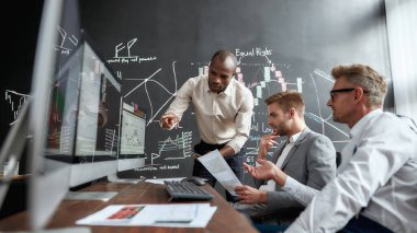 Bir Akıl Oyunu. Ofiste çalışırken bilgisayar ekranlarındaki grafiklere, indekslere ve numaralara bakan üç erkek tüccar. Yatay çekim. Web pankartı