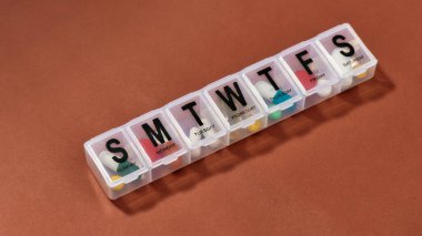 Haftalık ilaç dağıtıcısı, reçeteli haplar ve vitaminler beyaz bir ilaç kutusunda, terracotta arka planında. Sağlık, vitamin ve tedavi kavramı