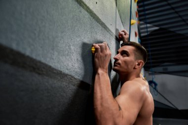 Kapalı alanda yapay tırmanma duvarı eğitimi alırken yukarı bakan bir adama yaklaş.